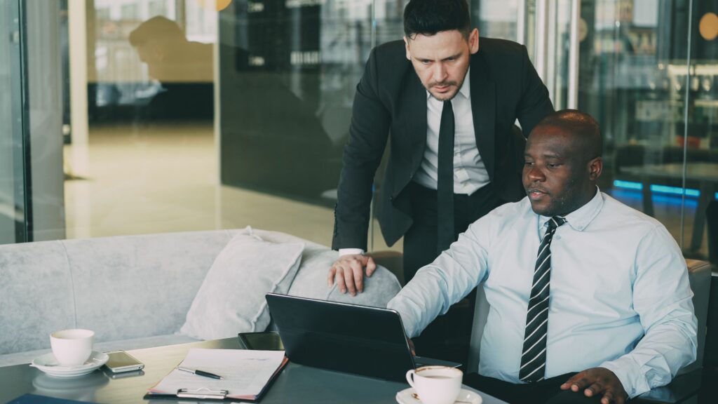 Two businessmen collaborating in a modern office, working on a laptop.